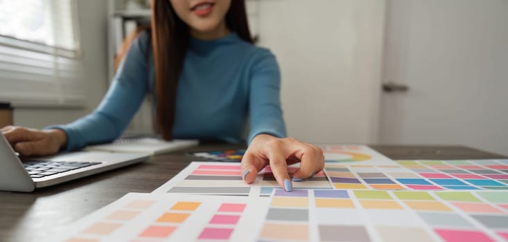 Focused on her color choices, the designer balances physical swatches and digital work, embodying the essence of creativity and design in a refined workspace.