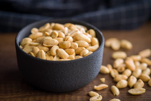 Roasted salted peanuts in bowl on a wooden table.
