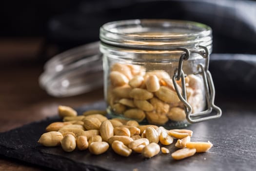Roasted salted peanuts in jar on a wooden table.