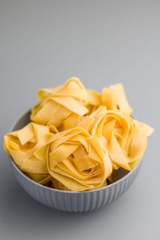 Italian pasta tagliatelle. Uncooked noodle pasta in bowl on a gray background.