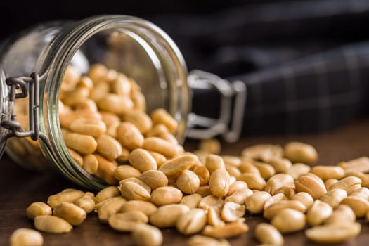 Roasted salted peanuts in jar on a wooden table.