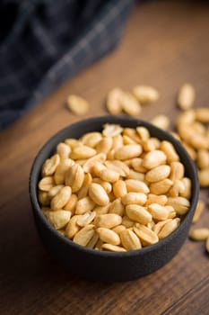 Roasted salted peanuts in bowl on a wooden table.