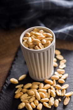 Roasted salted peanuts in cup on a wooden table.