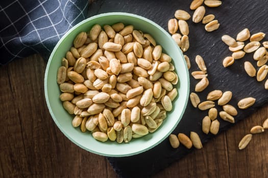 Roasted salted peanuts in bowl on a wooden table. Top view.