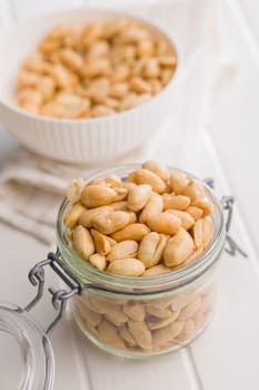Roasted salted peanuts in jar on a white table.