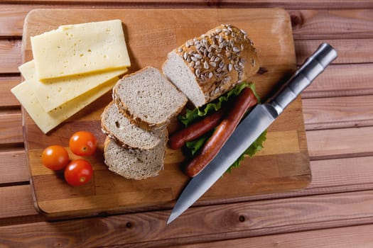 Fried sausages on green salad, bread, cherry tomatoes and cheese on wooden board, close up - top view