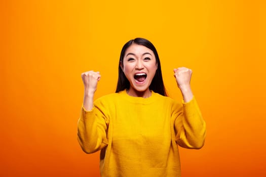 Excited young woman smiling confidently and celebrating her achievements with fists raised. Asian lady cheering with her arms and mouth wide open, feeling strong and optimistic, with triumphant look.