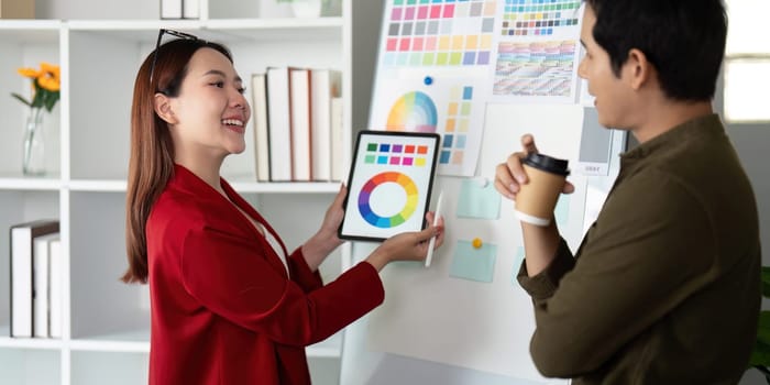 The female designer enthusiastically presents her color selections on a tablet, inviting input from her male colleague in a vibrant design office.