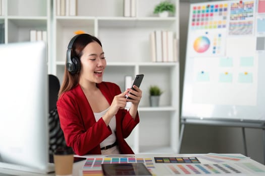In an inspiring workspace, a designer, equipped with headphones, joyfully interacts with her smartphone, showcasing a blend of creativity and focus.
