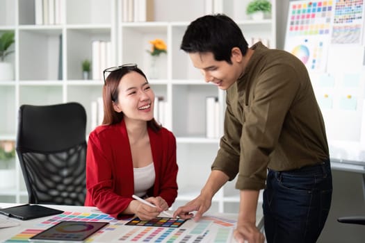 A male and female designer exchange ideas and laughter over a colorful design presentation, fostering teamwork and creativity.
