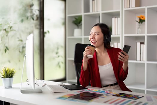 Savoring a moment of leisure, a designer enjoys her coffee while engaging with her smartphone in a bright, inspiring workspace.