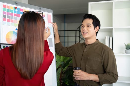 In a collaborative environment, a female designer makes adjustments on a color board as her male counterpart facilitates an engaging discussion about visual elements.