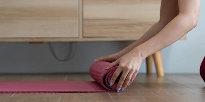 After a calming yoga practice, a woman rolls up her mat, representing peace and focus in her wellness journey.