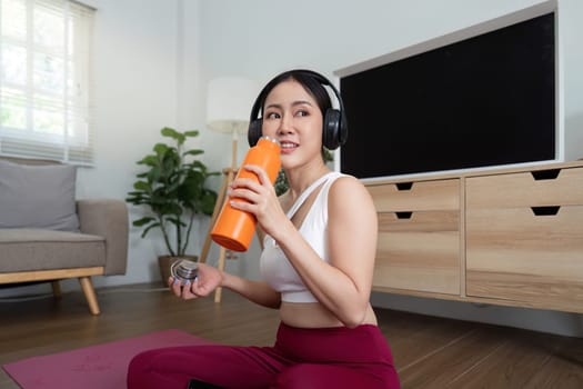 Taking a moment to hydrate, a fitness enthusiast enjoys her drink while listening to music, exemplifying the balance of exercise and relaxation.