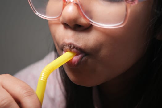 Girl enjoys a refreshing drink through a bright yellow straw indoors.