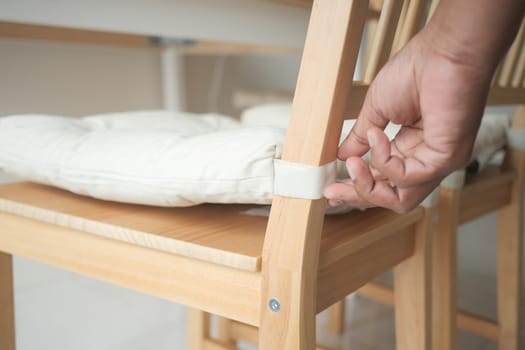 A hand secures a cushion to a wooden chair in a cozy interior space.