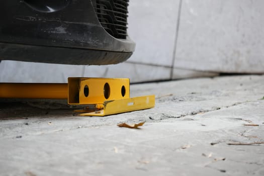 A yellow wheel clamp secures a car in an indoor parking area.