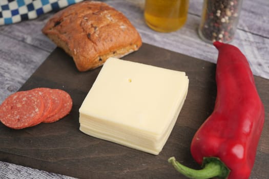 Fresh cheese, salami slices, and a pepper next to a crunchy roll.