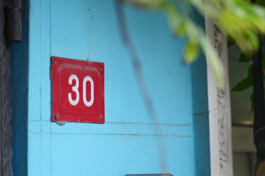 A red house number thirty displayed on a vibrant blue wall.