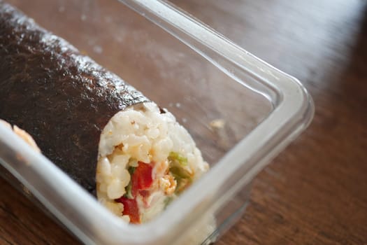 Fresh sushi roll filled with vegetables and seafood in a container