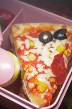A pizza slice features pepperoni, olives, and corn in a vibrant lunchbox.