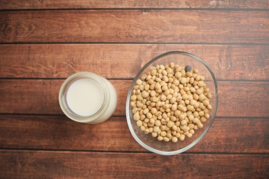 A glass bowl of soybeans alongside a jar of soy milk on a wooden table.