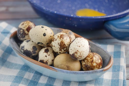 A bowl of assorted quail eggs rests on a blue checkered cloth.