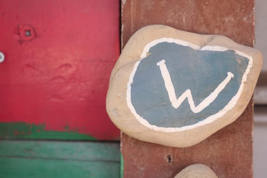 Blue and white letter W painted on a smooth rock beside red wall.