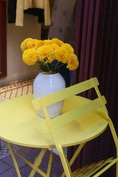 A vase of vibrant yellow flowers decorates a yellow table in a cafe.