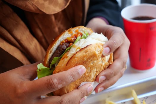 A person is savoring a juicy burger with fresh toppings and sauce.