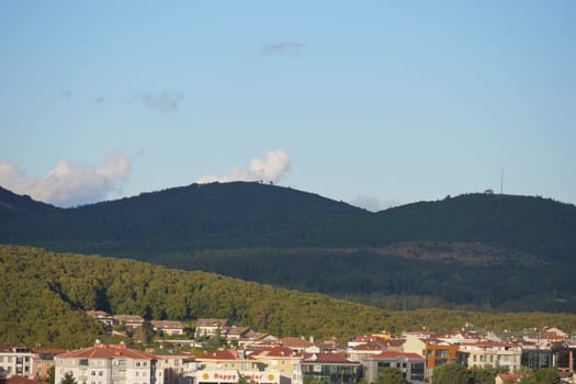 A view showcasing lush hills rising behind modern buildings under blue sky.