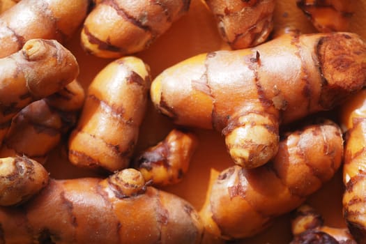 Curved orange turmeric roots are arranged closely, showcasing their texture.