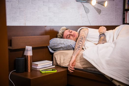 A handsome young man with blond hair and blue eyes is sleeping soundly in a modern bedroom. Soft morning light enters the room, creating a serene atmosphere as he rests.