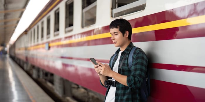 Standing next to a vibrant train, a young traveler interacts with his mobile device, illustrating the fusion of travel and technology in the modern age.