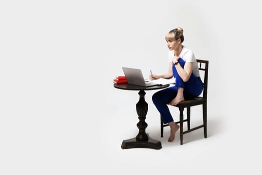 Focused young woman sitting at desk working or studying remotely writing notes while looking on the notebook laptop screen. Distant learning or remote work concept. Isolated on white background.