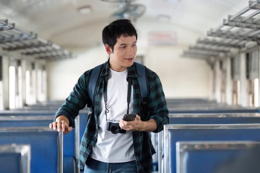 In a quiet train carriage, a young man stands with a camera, engaging with his phone to plan his next adventure, enjoying the serenity of travel.