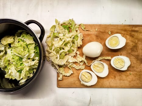 Freshly chopped cabbage sits next to sliced boiled eggs on a wooden cutting board in a kitchen.
