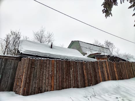 Snow blankets traditional structures and a wooden fence, capturing the tranquility of a winter day.