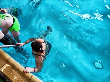 Individuals are swimming and engaging playfully in a bright indoor pool while enjoying a sunny afternoon together.