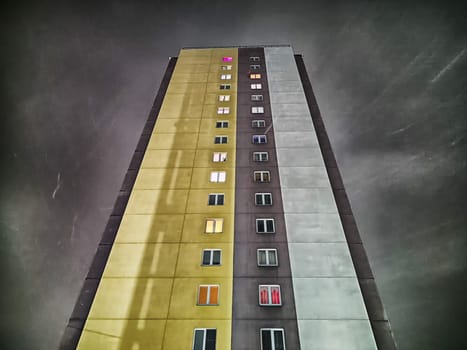 A tall residential building stands prominently against a stormy sky, showcasing multiple colorful windows and gloomy weather.
