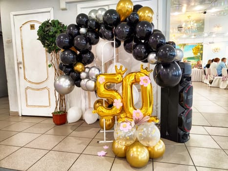 Festive setup features black, gold, and silver balloons along with large golden numbers celebrating a milestone birthday inside a decorated hall.