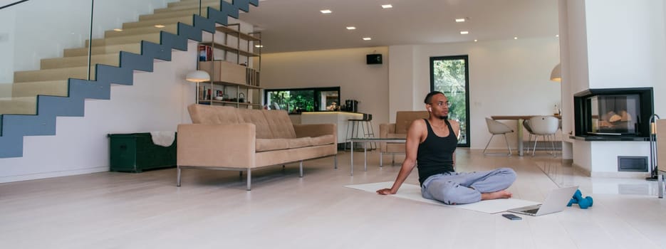 Training At Home. Sporty African American man doing the training while watching an online tutorial on a laptop, exercising in the living room, free space.