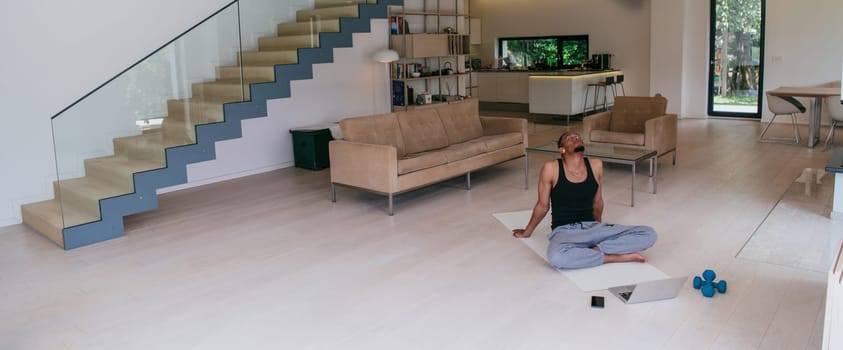 Training At Home. Sporty African American man doing the training while watching an online tutorial on a laptop, exercising in the living room, free space.