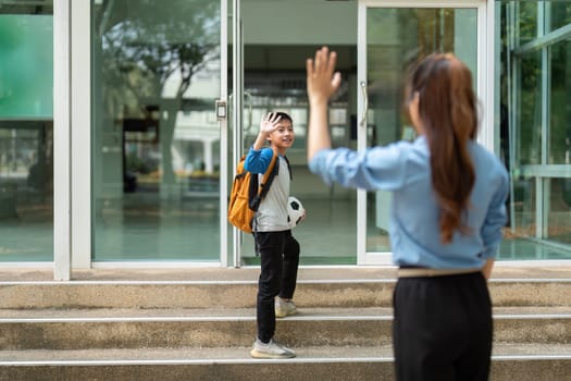As her son waves back at her, a sense of pride fills the mother's heart, highlighting their close relationship as he heads confidently to school.