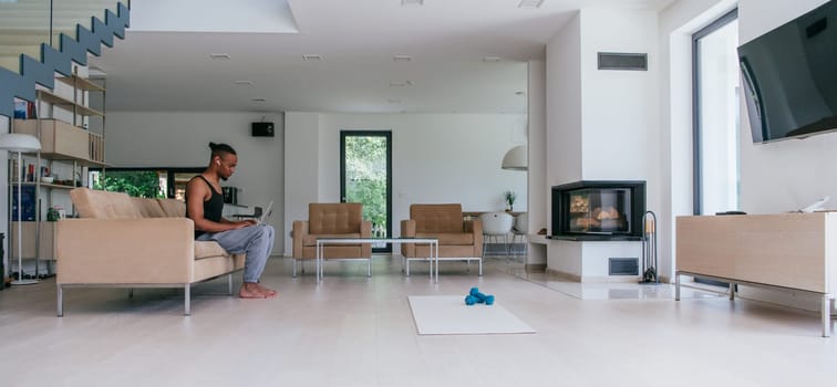 African American man in glasses sitting at a table in a modern living room, using a laptop for business video chat, conversation with friends and entertainment