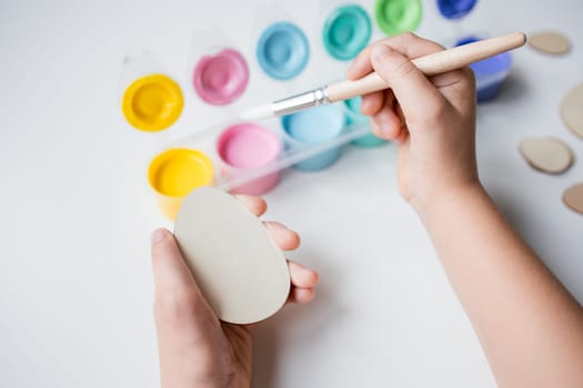 Child painting Easter wooden egg with bright colors and brush for creative art project.