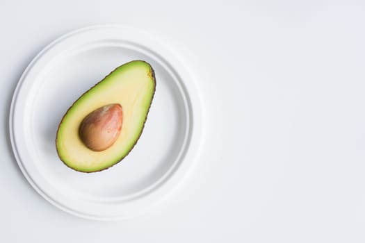 Halved avocado on white plate against minimalist white background.