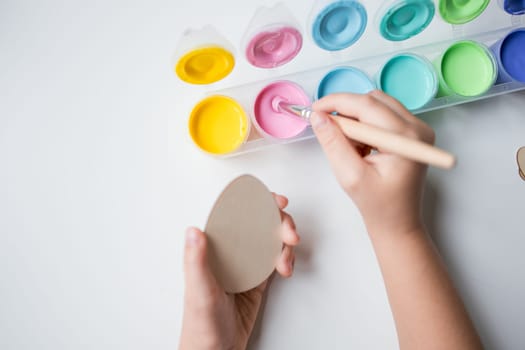 Child painting Easter egg with pastel acrylic colors on white table.