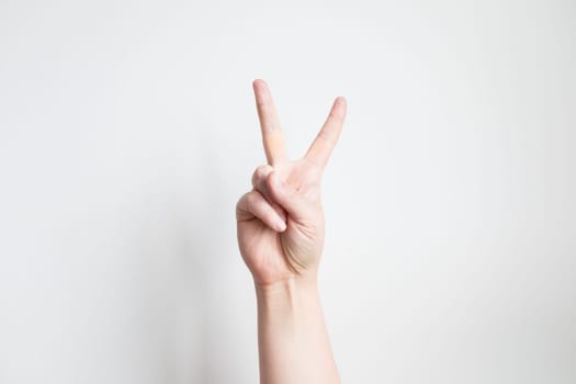 Caucasian adult hand making peace sign gesture against white background.