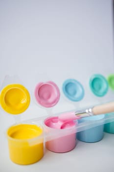 Colorful paint pots with brush in pastel shades.